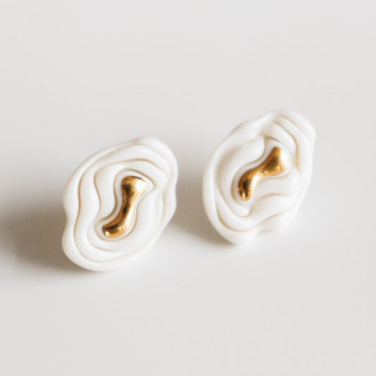 Pair of white earrings with gold accents on a light gray background