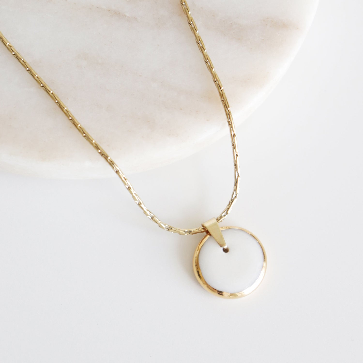 Gold necklace with a circular pendant on a light background