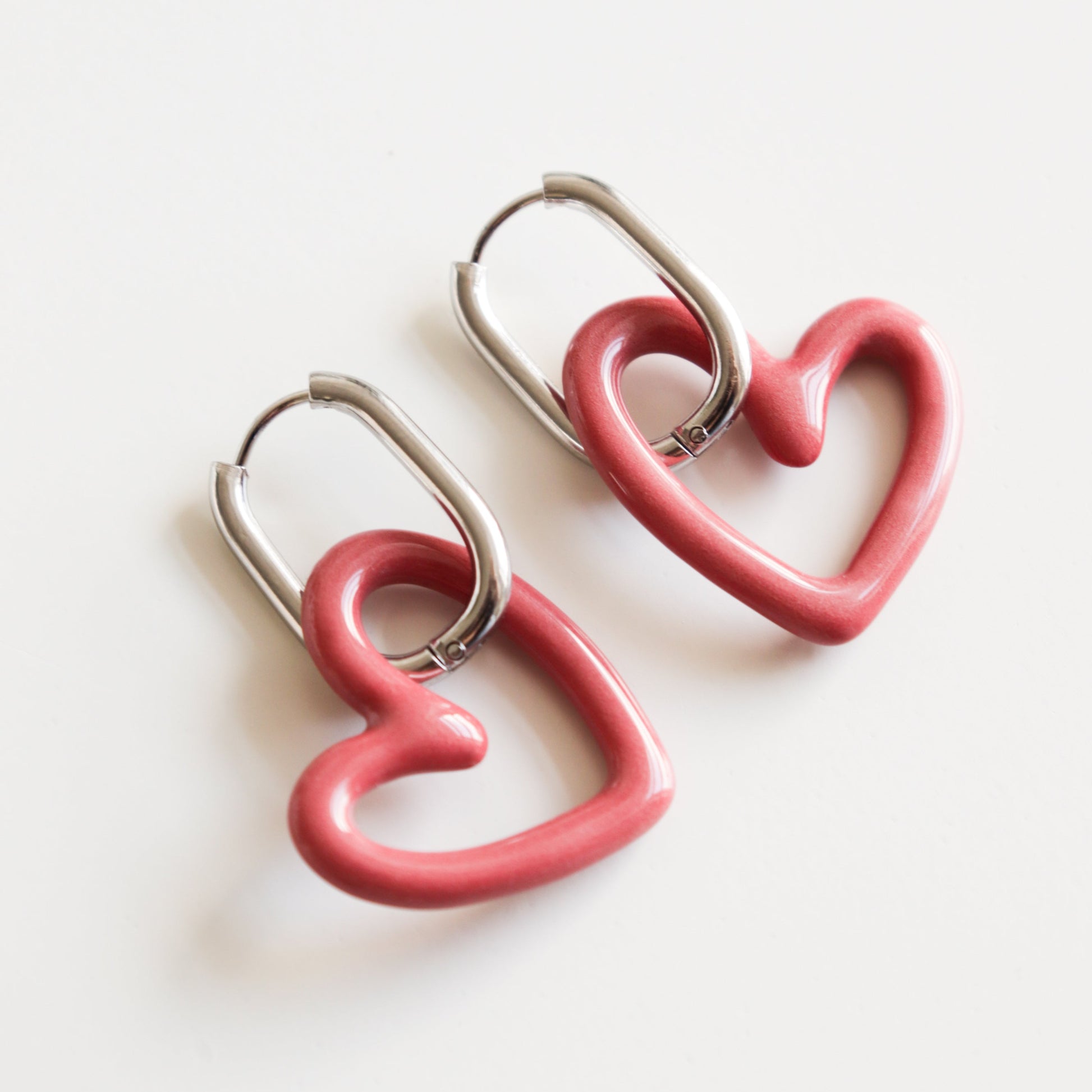 The Heart Earrings by Rozenthal Jewelry are lightweight, waterproof silver hoops with pink, heart-shaped charms, shown on a white background.