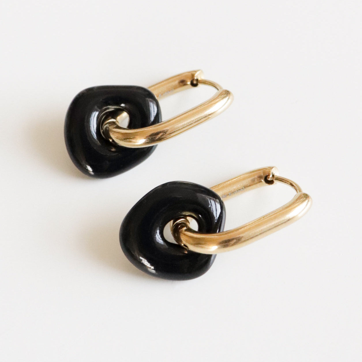 Pair of gold hoop earrings with black charms on a white background