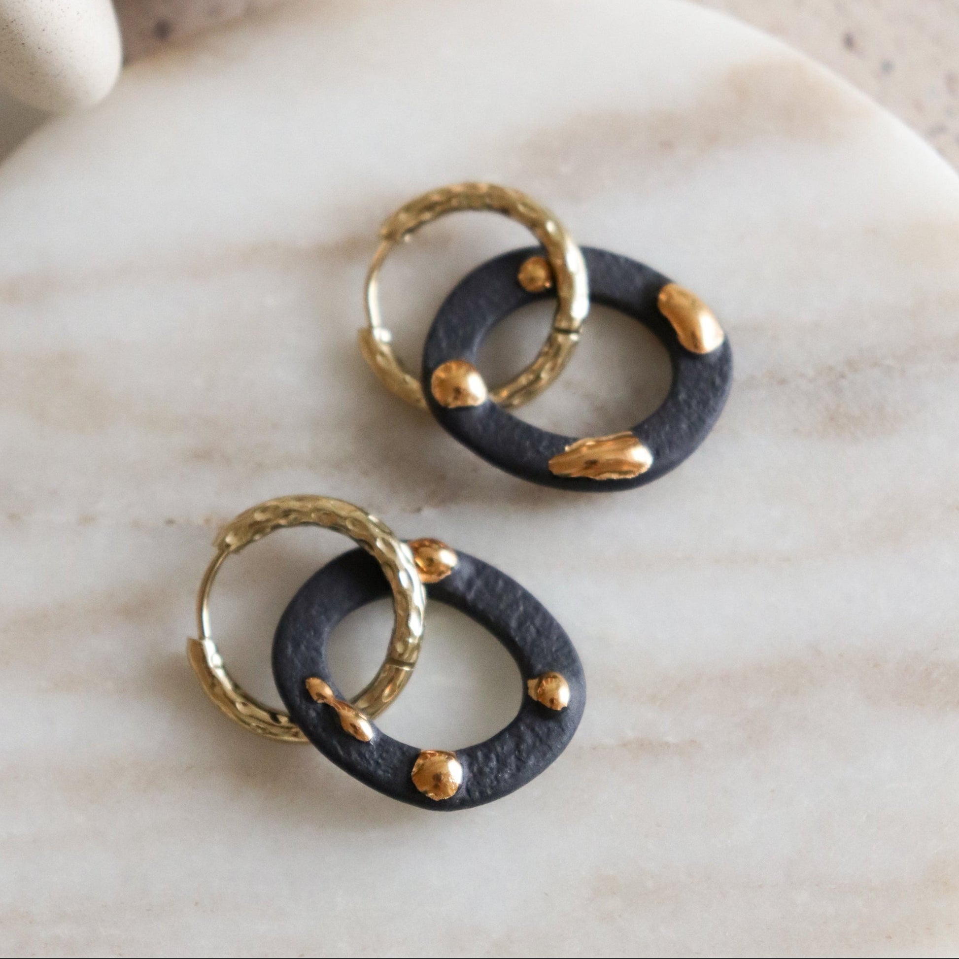 Pair of earrings with black and gold circular design on a marble surface
