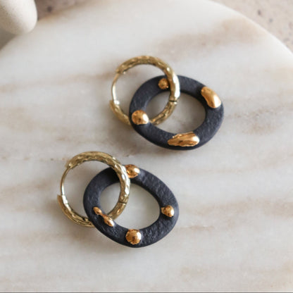 Pair of earrings with black and gold circular design on a marble surface