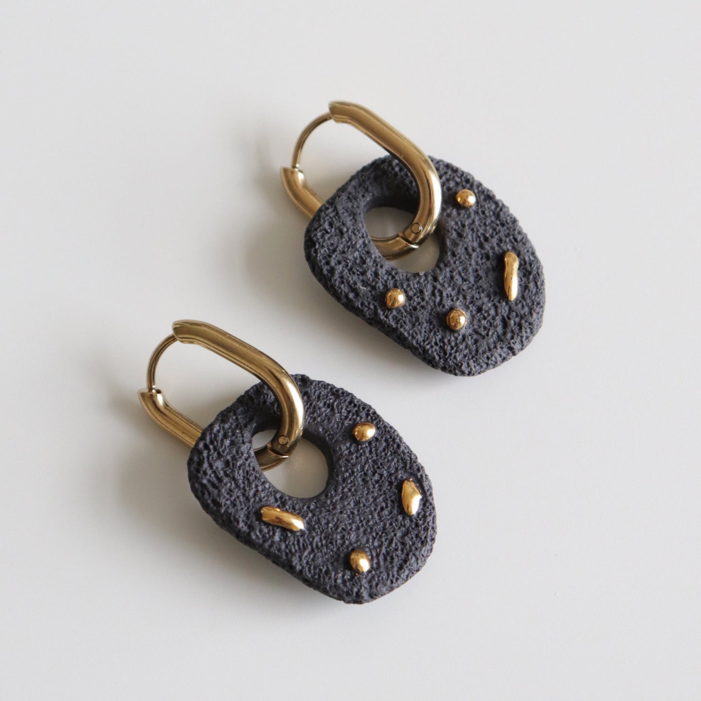 A pair of textured black  and gold hoop earrings on a light gray background.