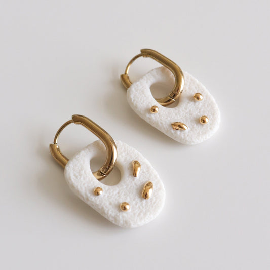 A pair of white textured drop earrings with gold hoops displayed on a clean light gray background.