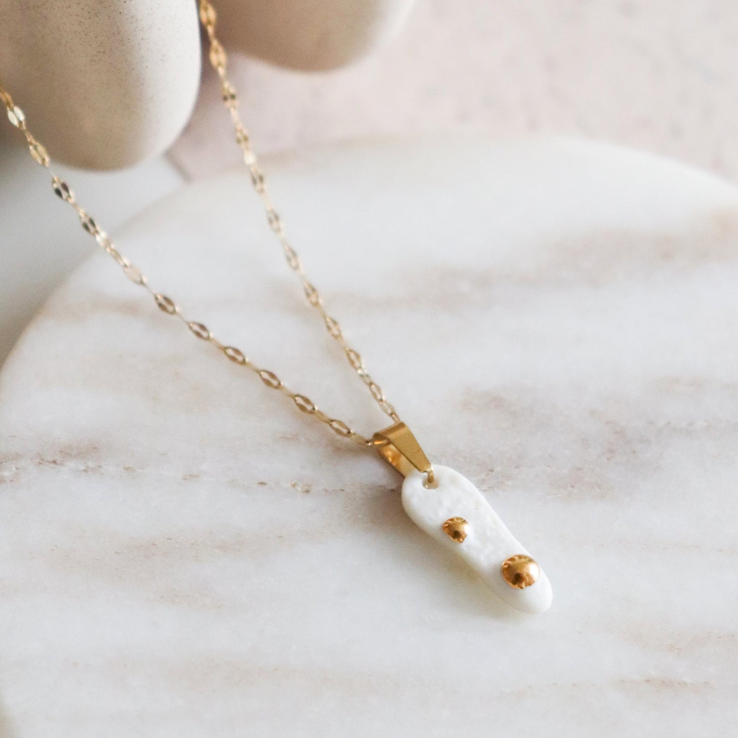 Gold necklace with a white pendant on a marble surface