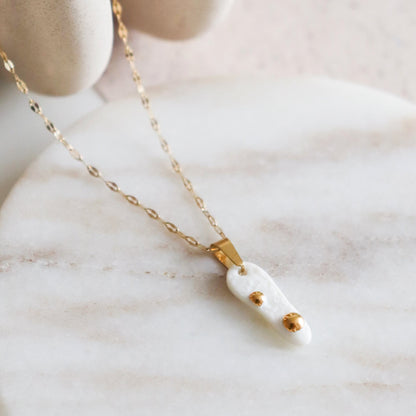 Gold necklace with a white pendant on a marble surface