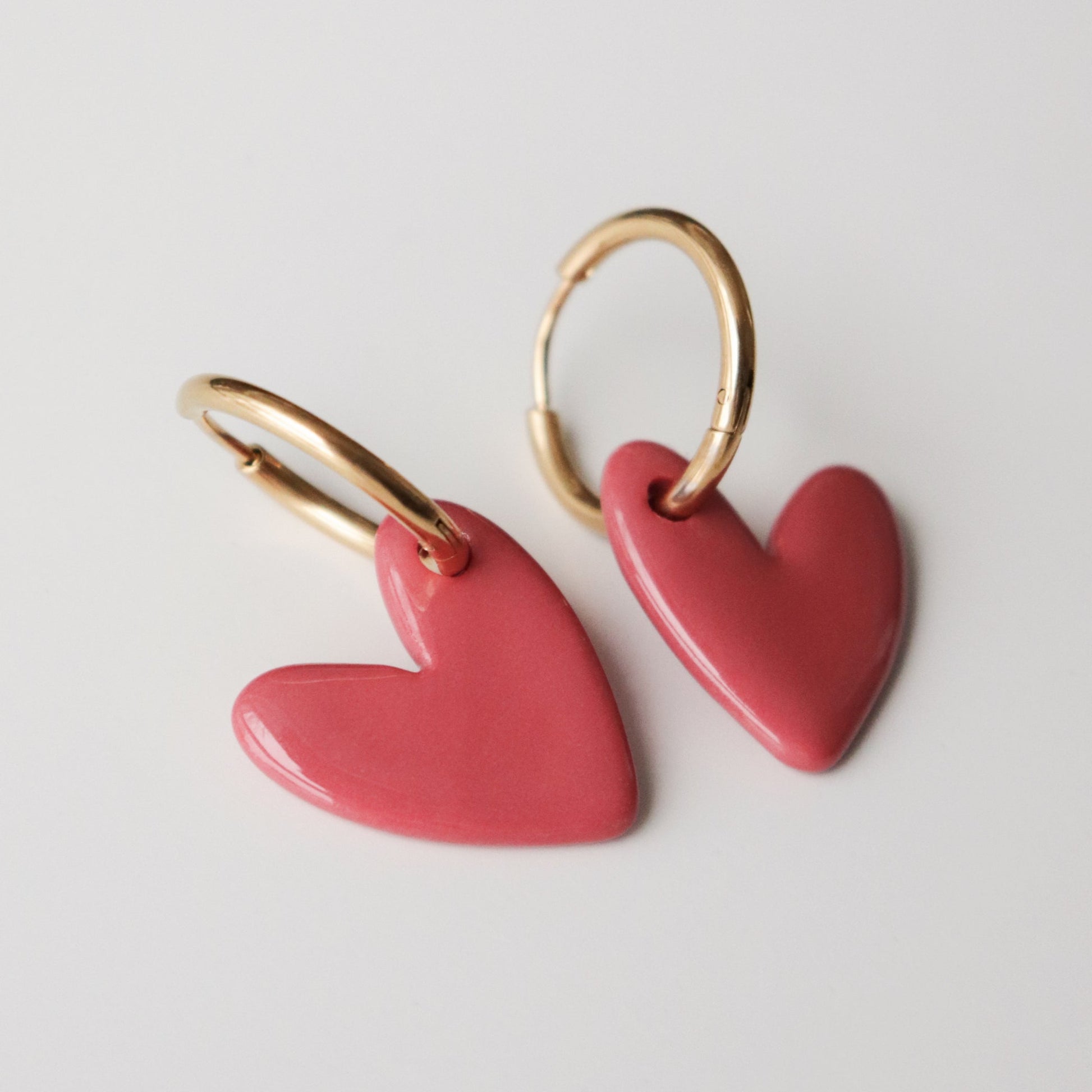 Pink heart-shaped earrings with gold hoops on a light gray background