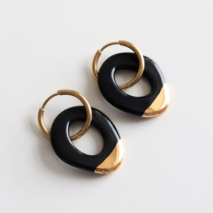 Pair of earrings in black with a gold dip and circular design on a light gray background