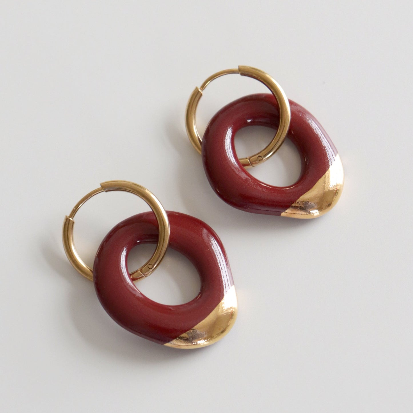 Pair of earrings with gold and burgundy circular designs on a light gray background