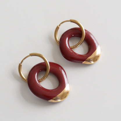 Pair of earrings with gold and burgundy circular designs on a light gray background