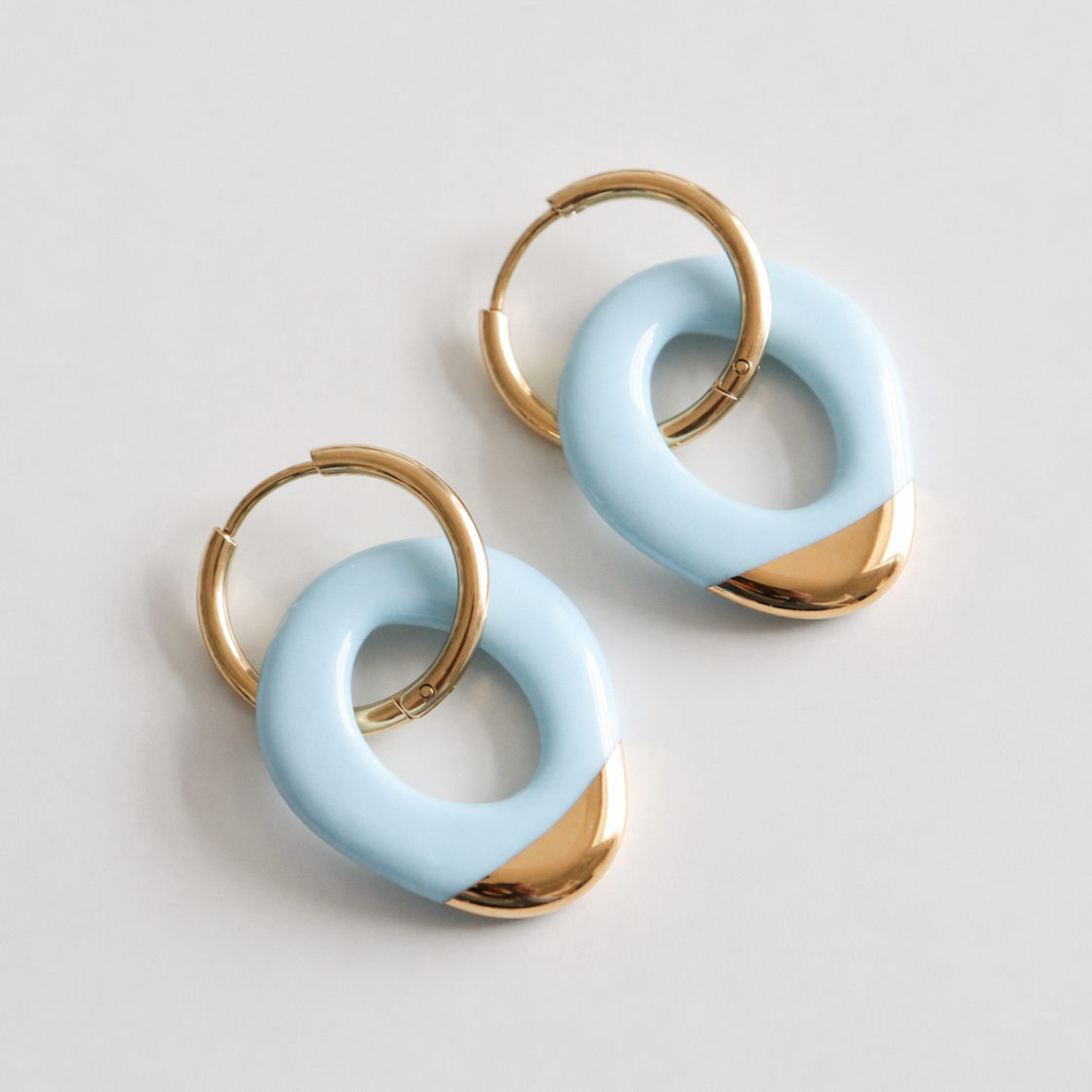 Pair of earrings with gold and light blue circular designs on a light gray background
