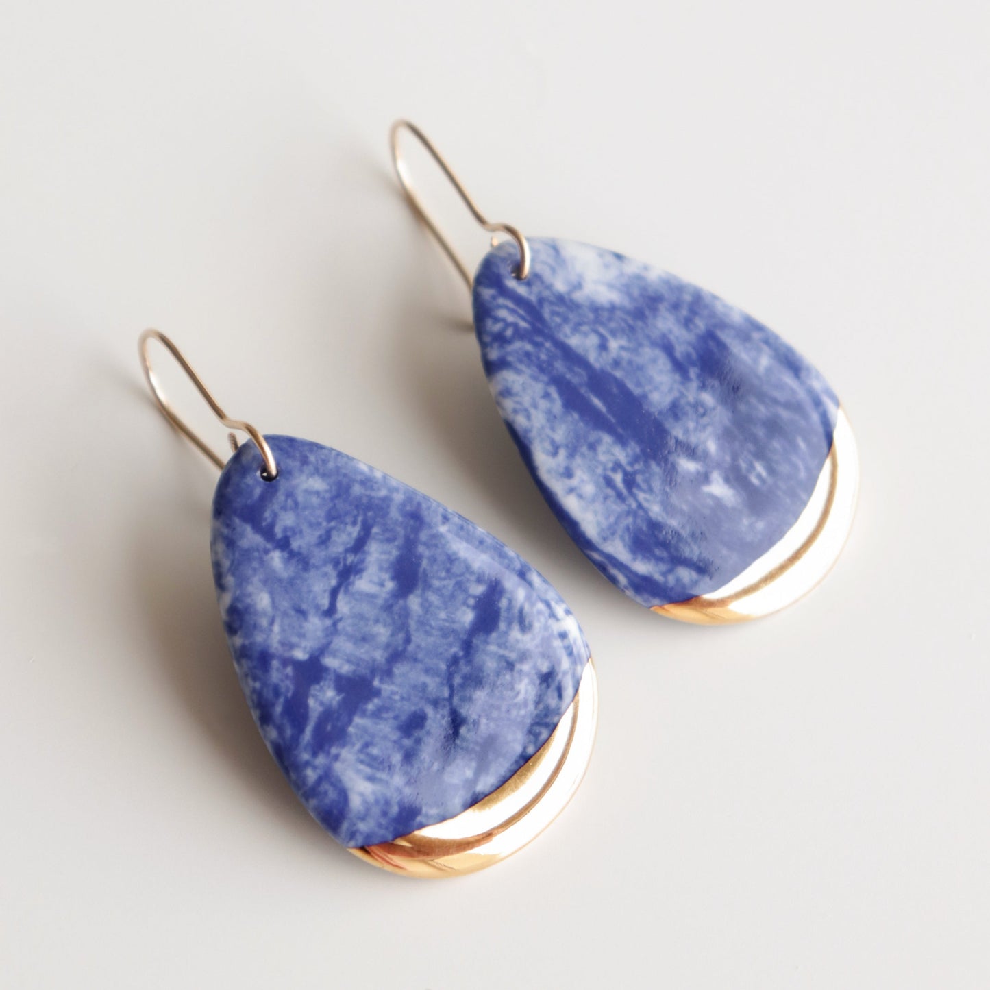 Blue marble teardrop earrings with gold accents on a light gray background