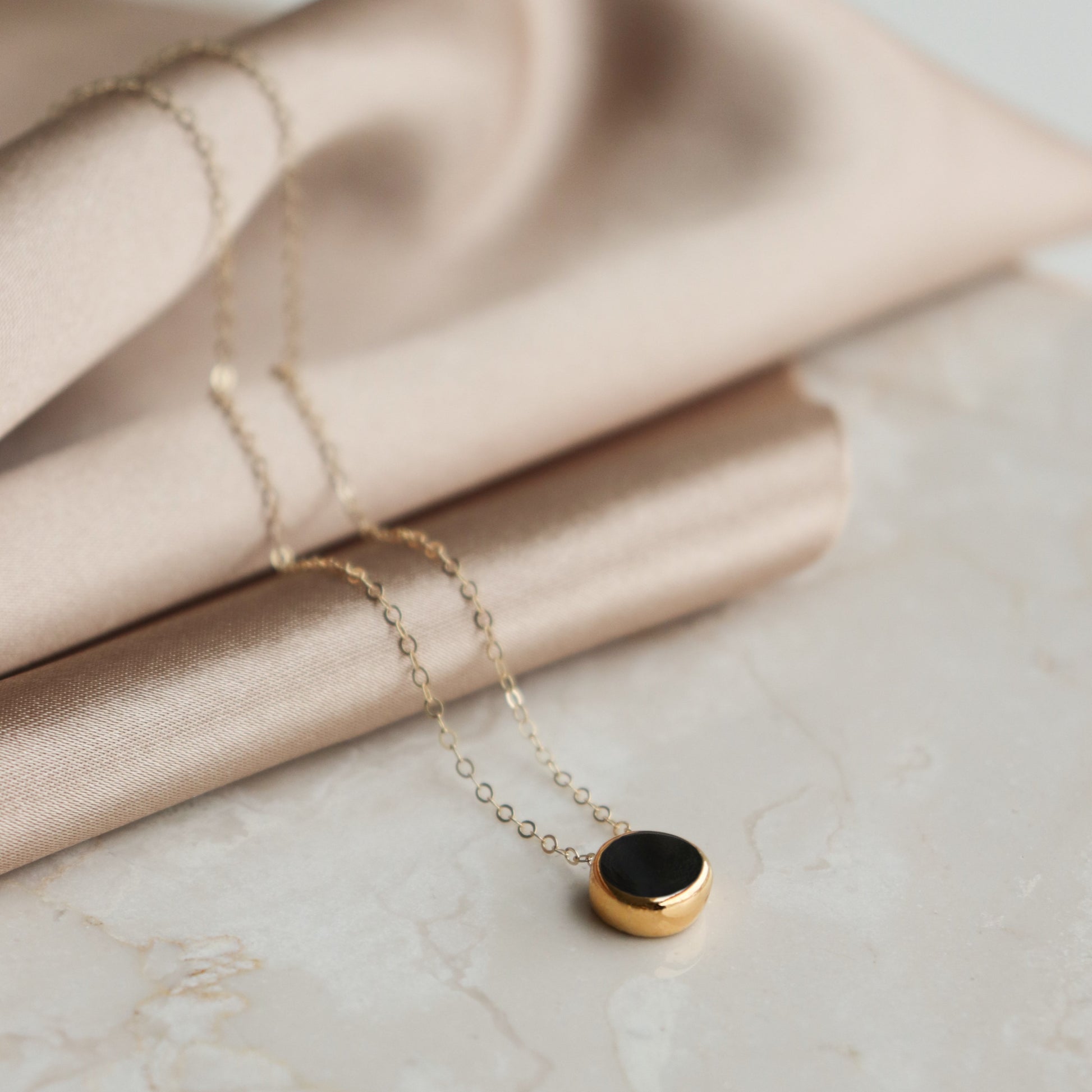 Gold necklace with a black pendant on a beige fabric background