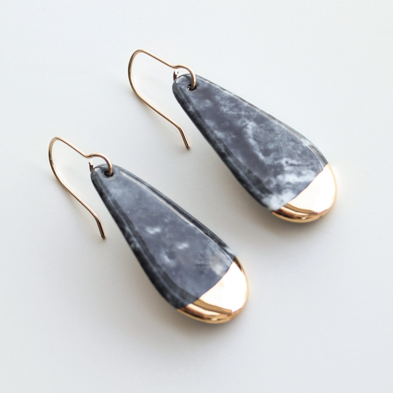 Drop earrings / S by Rozenthal Jewelry: teardrop-shaped, handmade in Latvia with marbled gray bodies and shiny gold tips on thin gold hooks, shown against a light background.