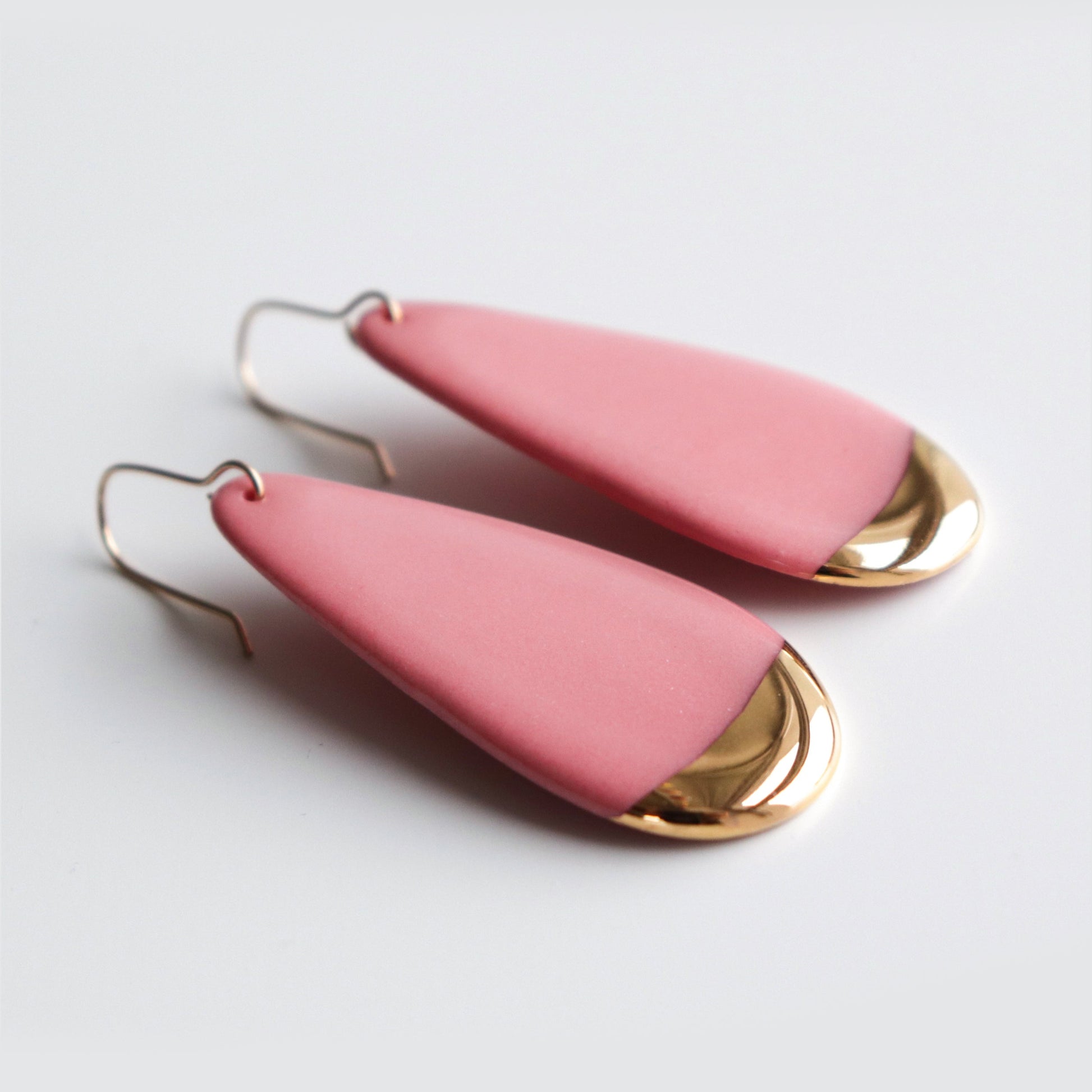 Pink teardrop earrings with gold accents on a light gray background