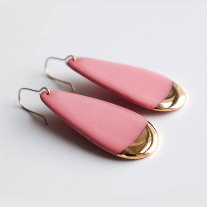 Pink teardrop earrings with gold accents on a light gray background