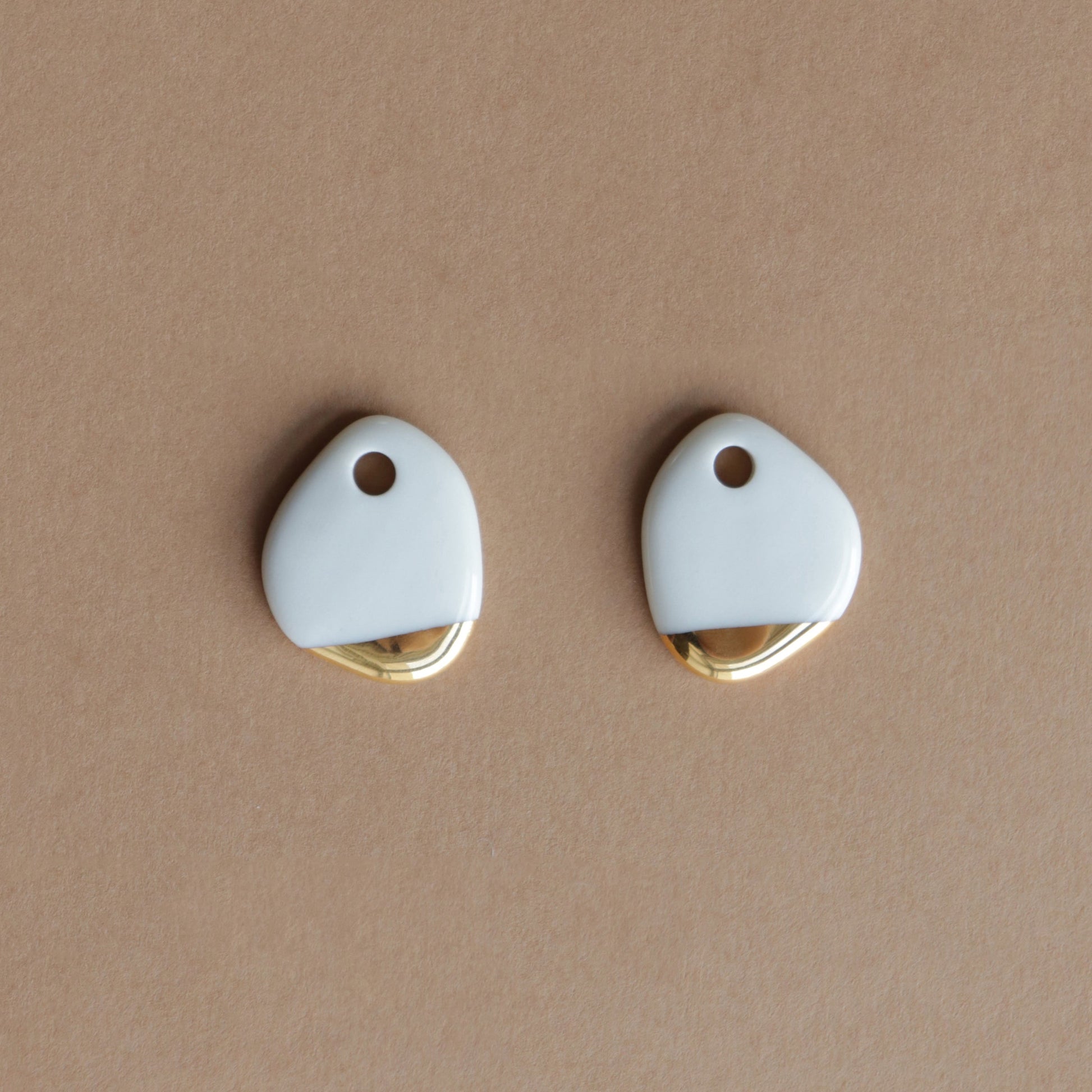The Arp Pearl Hoops by Rozenthal Jewelry are uniquely shaped white porcelain pendants with gold accents, each with a small top hole—ideal for fans of distinctive handmade jewelry.