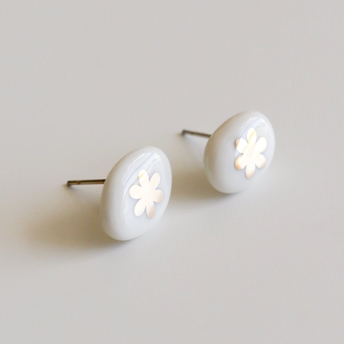 A pair of oval stud earrings with a glossy white finish and a small white flower cutout in the center, set against a plain light gray background.