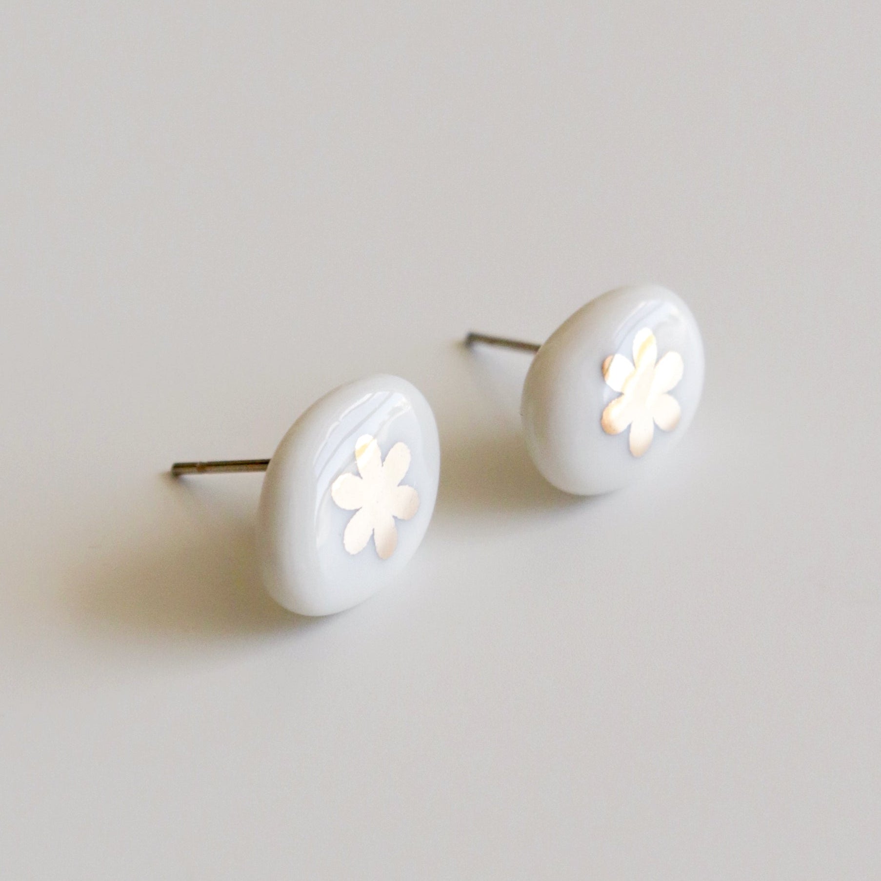 A pair of oval stud earrings with a glossy white finish and a small white flower cutout in the center, set against a plain light gray background.