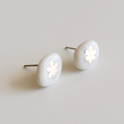 A pair of oval stud earrings with a glossy white finish and a small white flower cutout in the center, set against a plain light gray background.