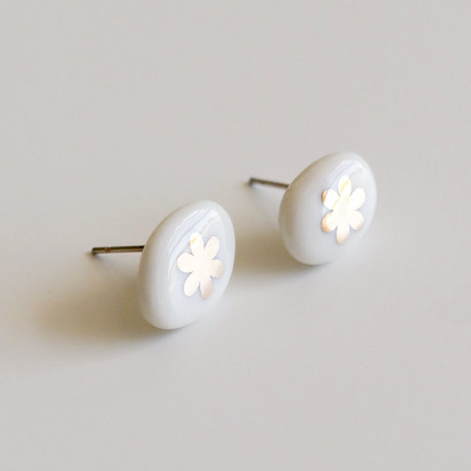 A pair of oval stud earrings with a glossy white finish and a small white flower cutout in the center, set against a plain light gray background.