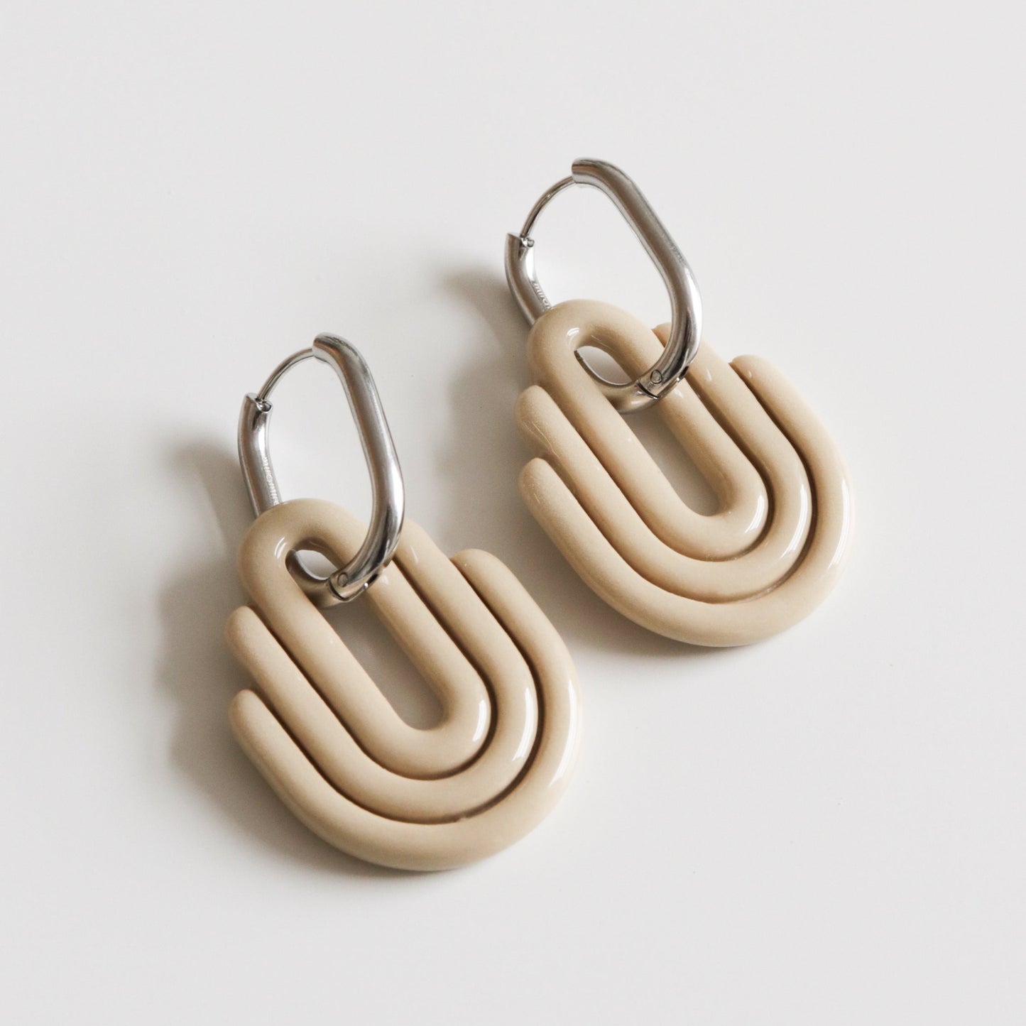 Pair of beige hoop earrings with silver hoops on a light gray background