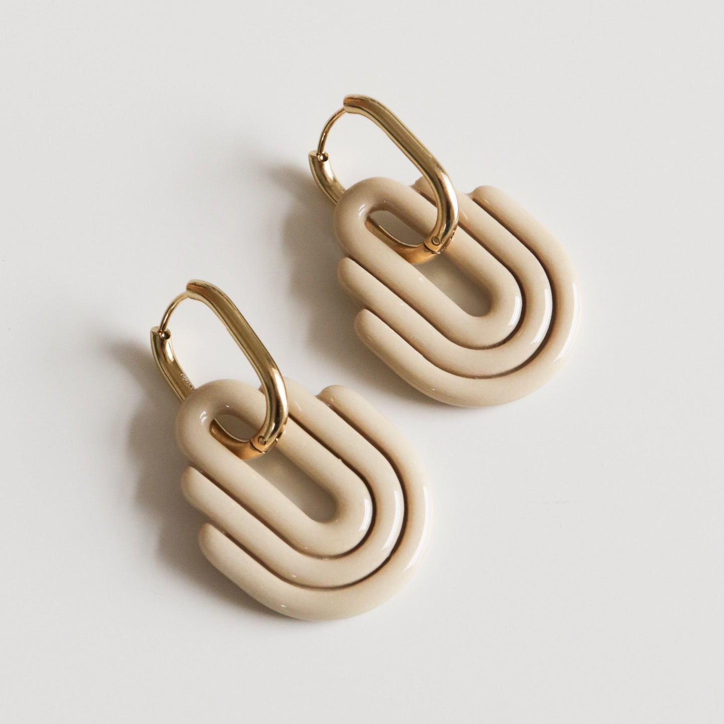 Pair of beige earrings with gold hoops on a light gray background