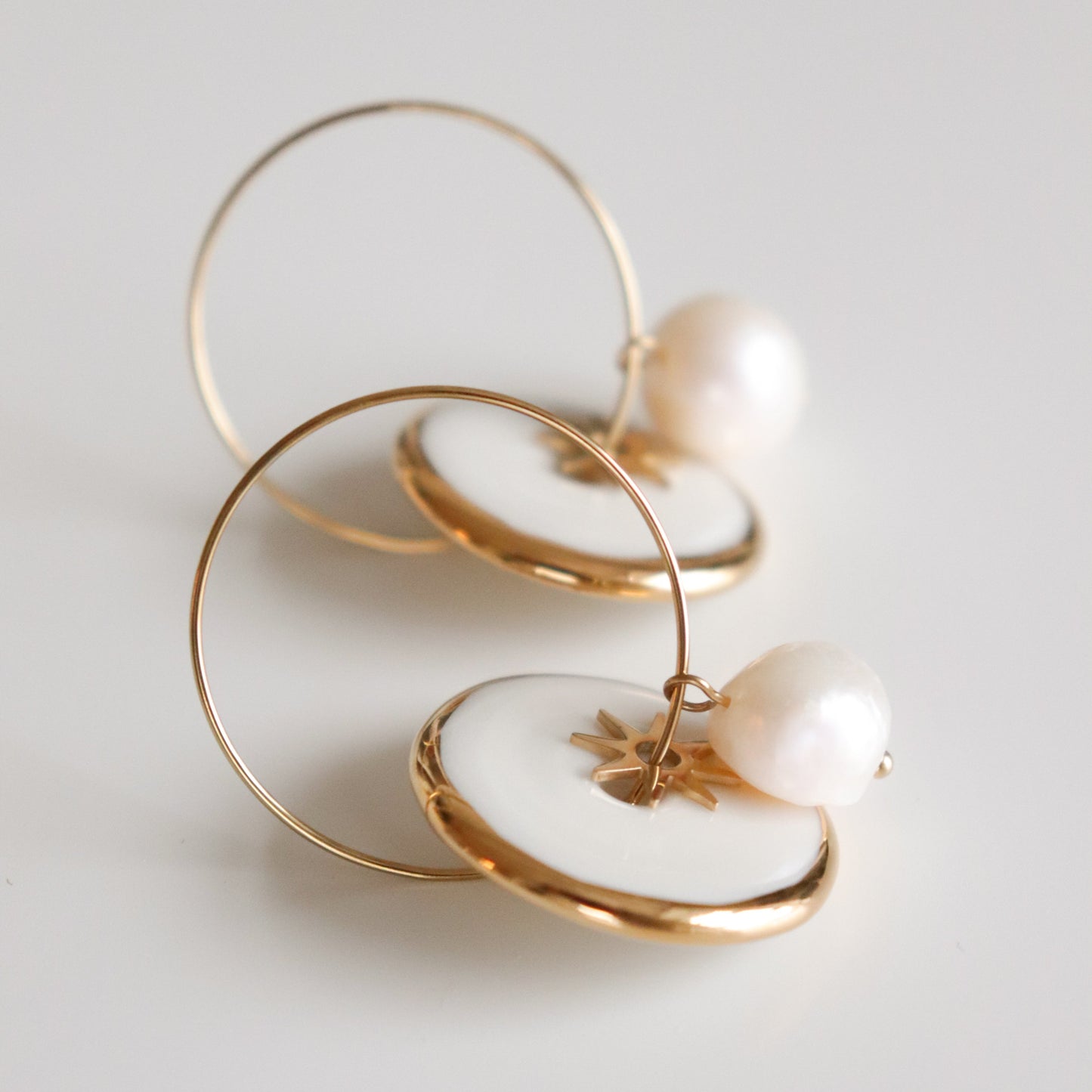 Gold hoop earrings with pearls and star elements on a light gray background