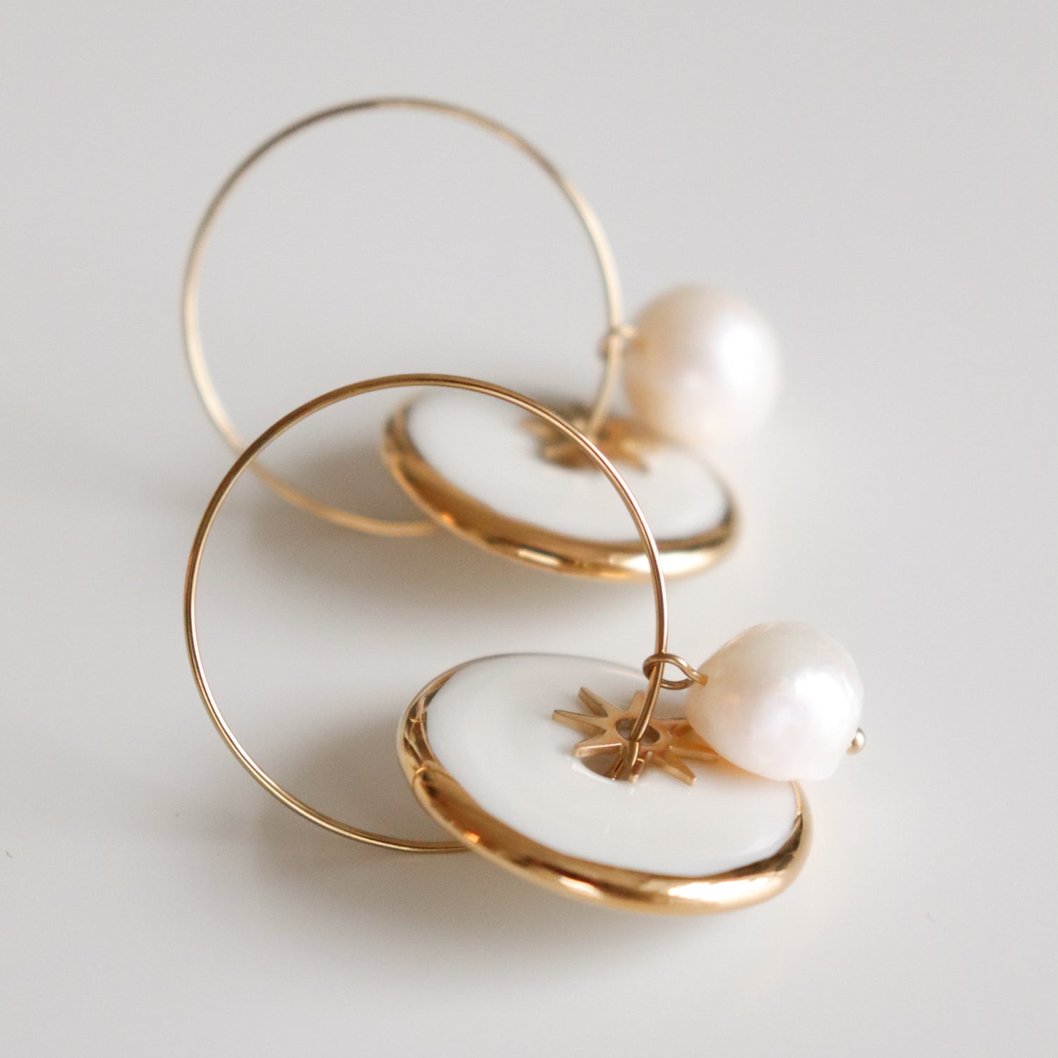 Gold hoop earrings with pearls and star elements on a light gray background