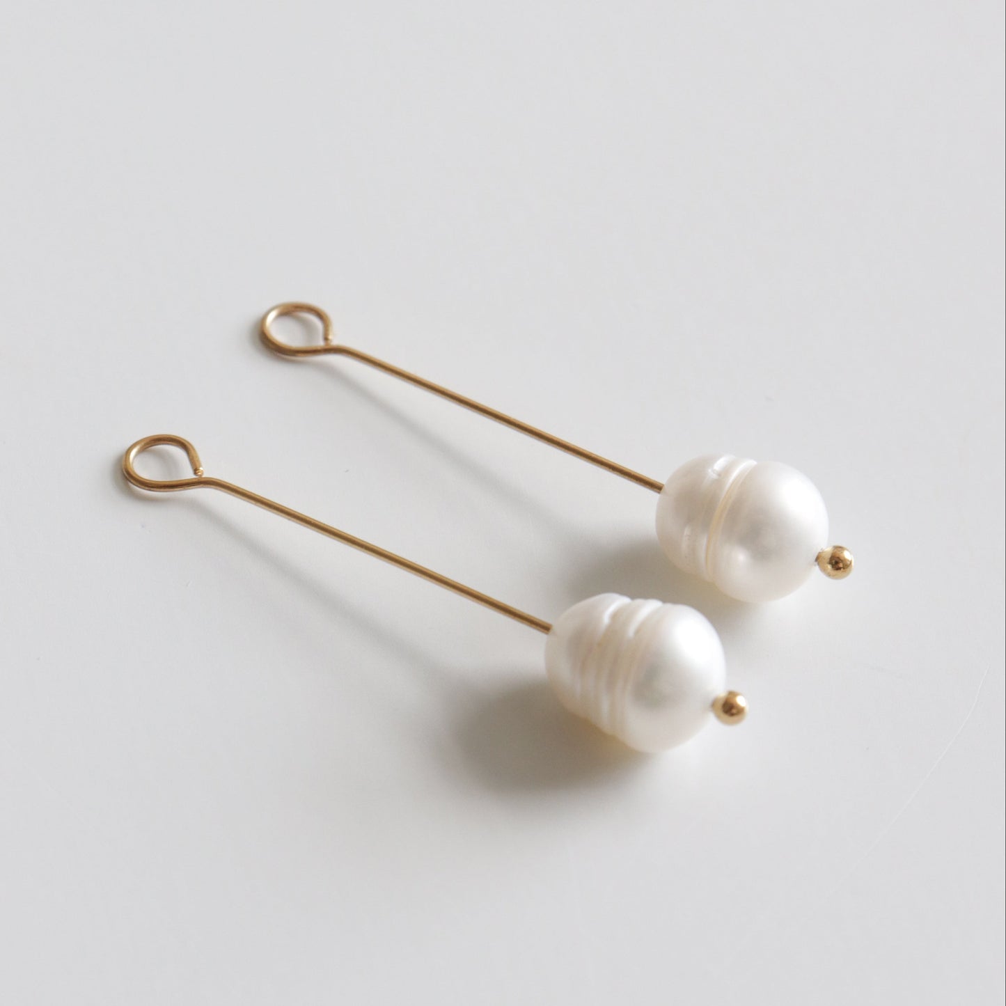 Pearl earrings with gold pin on a light gray background