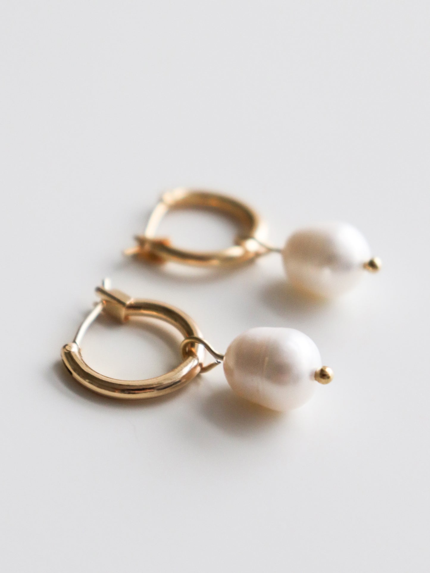 Gold hoop earrings with pearl drops on a light gray background