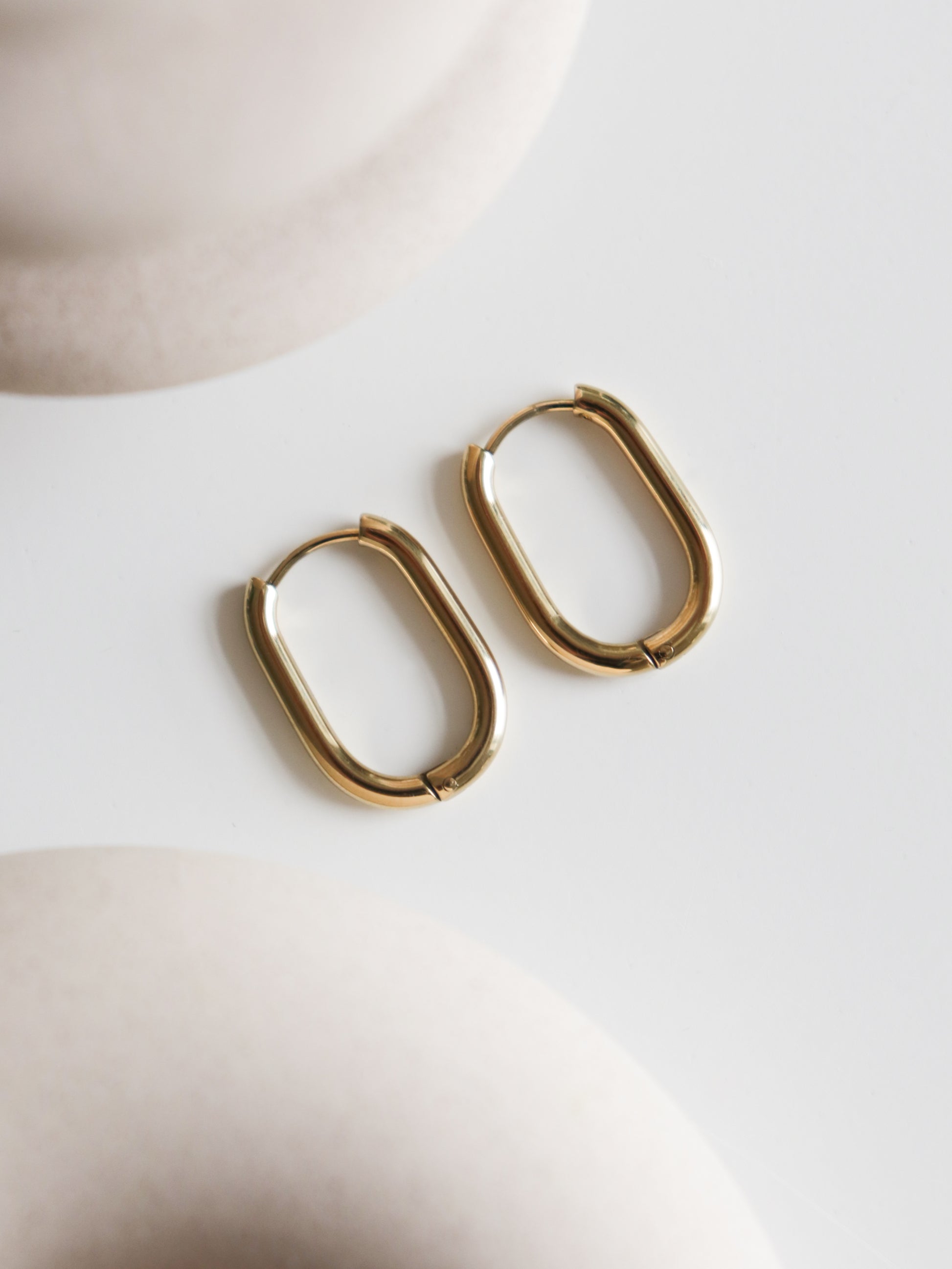 A pair of Large Hoops by Rozenthal Jewelry rests on a smooth white surface, with soft beige shapes blurred in the foreground and background.