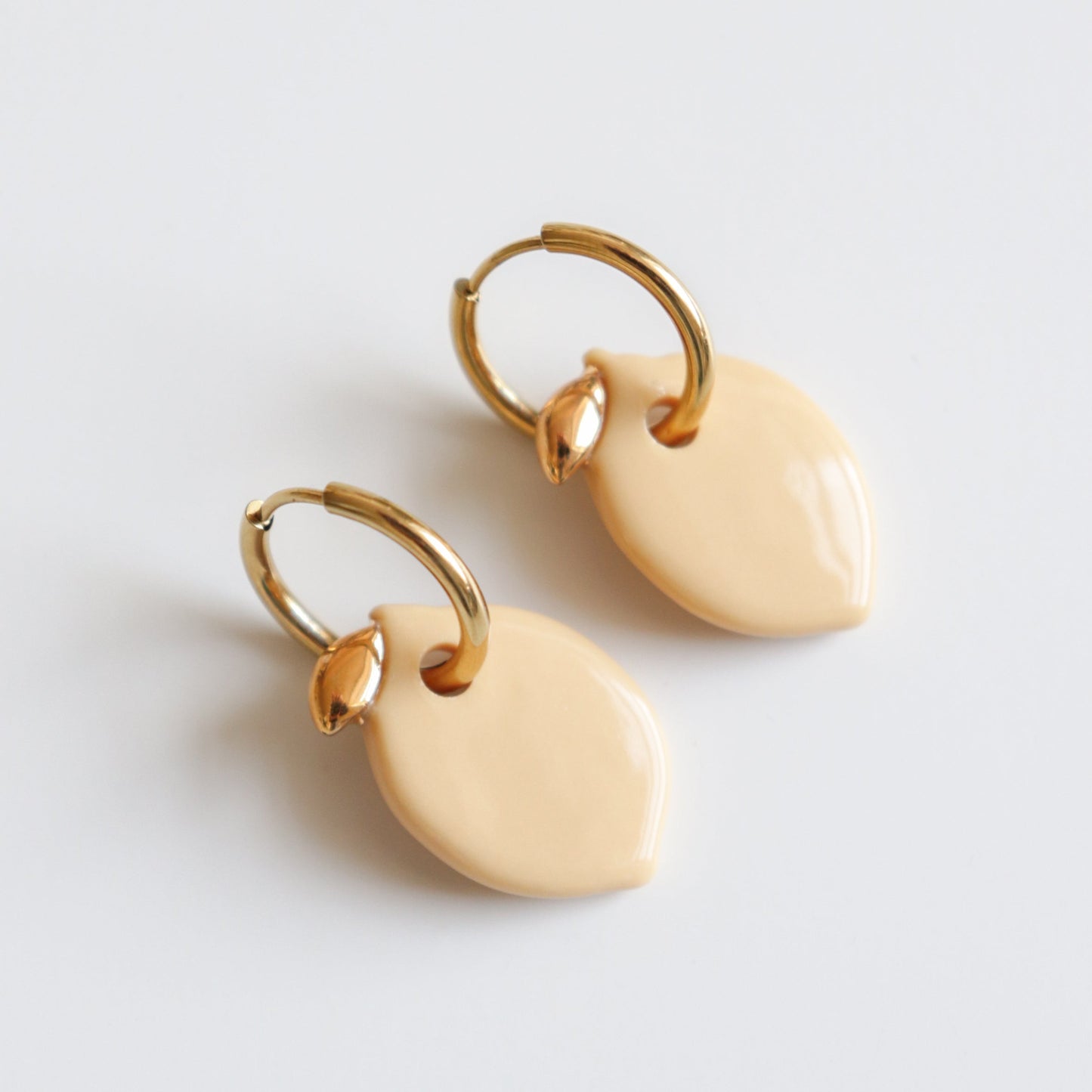 Pair of gold hoop earrings with lemon charms on a light gray background