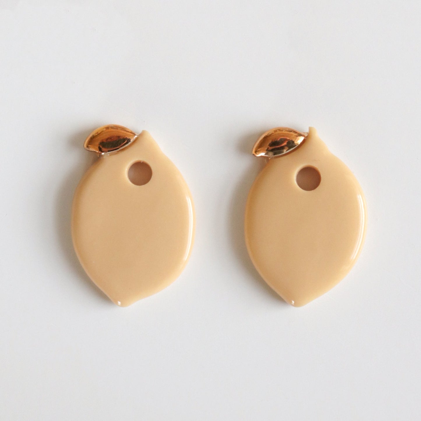 Two beige lemon charms with gold accents on a light gray background