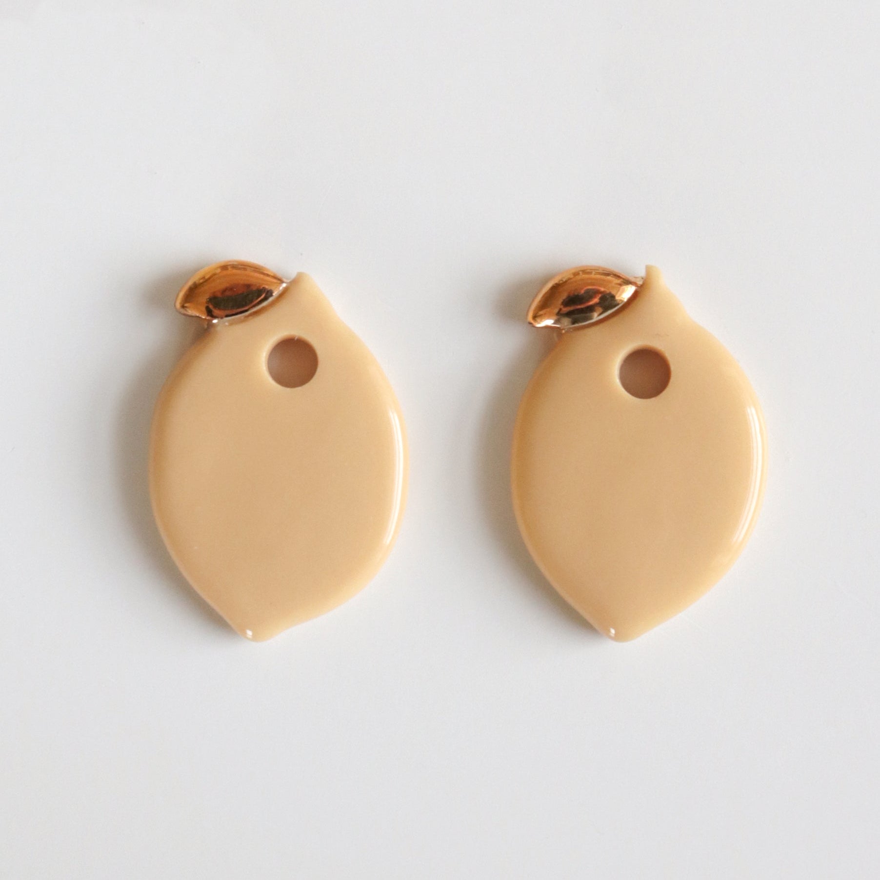 Two beige lemon charms with gold accents on a light gray background