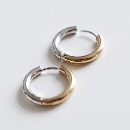 Two Gold and Silver Hoops by Rozenthal Jewelry rest side by side on a white surface; each earring features a smooth, shiny finish with half silver and half gold tones.